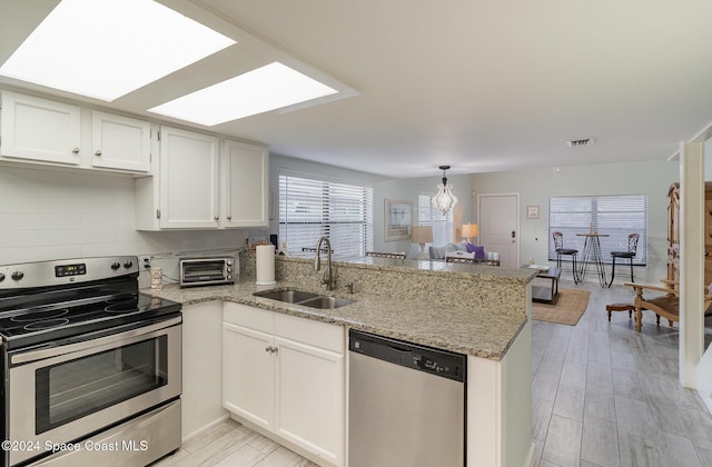 kitchen with sink, kitchen peninsula, appliances with stainless steel finishes, white cabinets, and light wood-type flooring