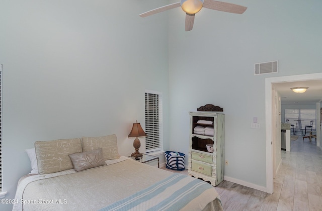 bedroom with a towering ceiling, light wood-type flooring, and ceiling fan