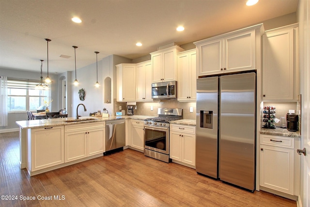 kitchen featuring kitchen peninsula, appliances with stainless steel finishes, sink, decorative light fixtures, and light hardwood / wood-style flooring