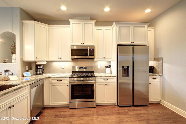 kitchen featuring decorative backsplash, light hardwood / wood-style floors, light stone countertops, and appliances with stainless steel finishes