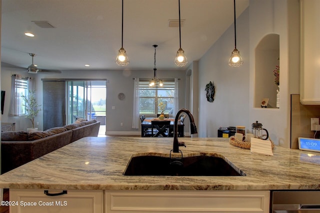 kitchen with white cabinets, decorative light fixtures, light stone counters, and sink