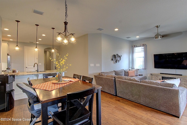 dining room with ceiling fan with notable chandelier, light hardwood / wood-style flooring, and sink