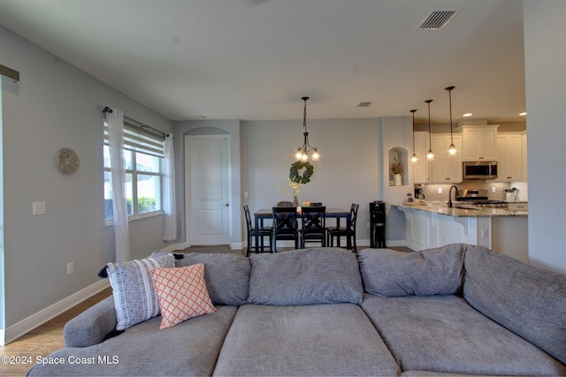 living room featuring sink, light hardwood / wood-style flooring, and an inviting chandelier