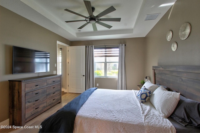 bedroom featuring ceiling fan, a tray ceiling, and light hardwood / wood-style flooring