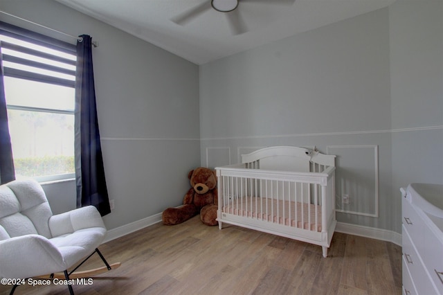 bedroom with a crib, light hardwood / wood-style flooring, and ceiling fan