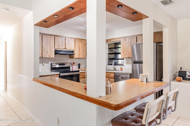 kitchen with sink, light tile patterned floors, tasteful backsplash, kitchen peninsula, and stainless steel appliances