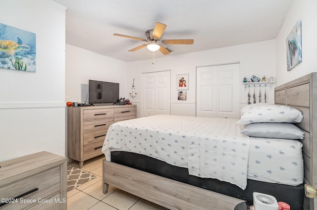 bedroom with a textured ceiling, ceiling fan, multiple closets, and light tile patterned flooring