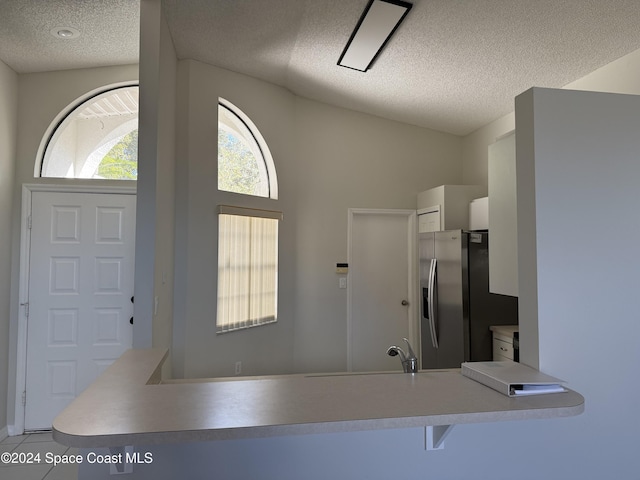 interior space with vaulted ceiling, stainless steel fridge, light tile patterned floors, a textured ceiling, and kitchen peninsula