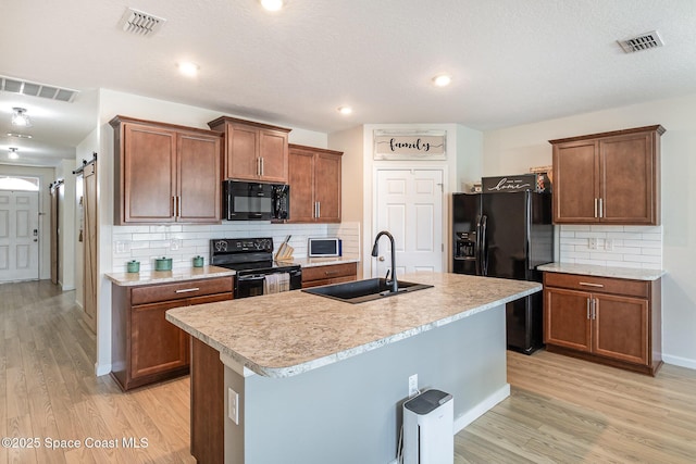 kitchen with tasteful backsplash, a barn door, an island with sink, and black appliances