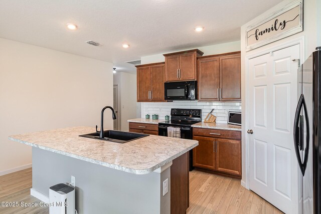 kitchen with backsplash, a kitchen island with sink, black appliances, sink, and light hardwood / wood-style flooring