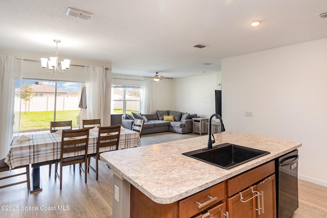 kitchen featuring dishwasher, ceiling fan with notable chandelier, sink, an island with sink, and decorative light fixtures