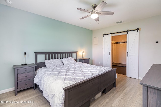 bedroom with ceiling fan, a barn door, and light hardwood / wood-style floors