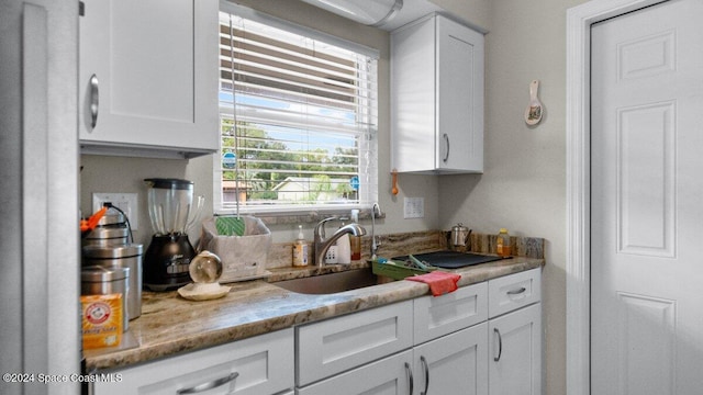 kitchen with light stone counters, sink, and white cabinets