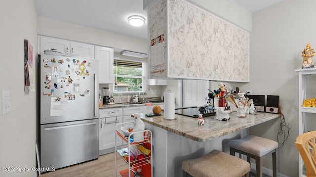 kitchen with stainless steel fridge, light stone countertops, white cabinetry, and a breakfast bar area