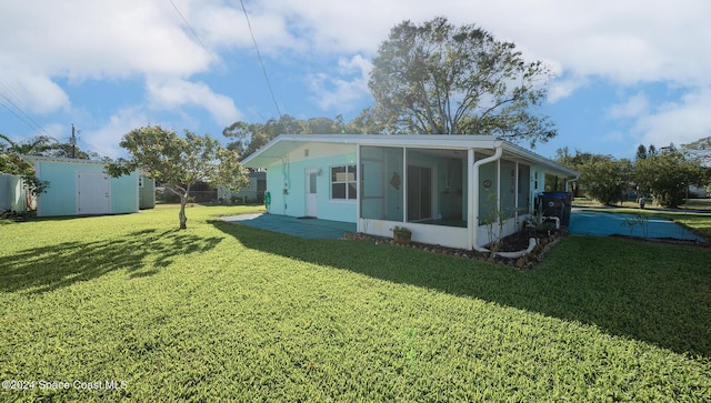 rear view of property with a lawn, a sunroom, and a shed