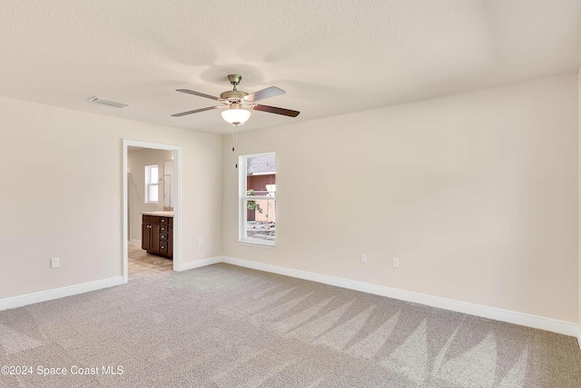 empty room with ceiling fan, light colored carpet, and a textured ceiling