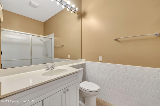 bathroom with tile patterned floors, toilet, vanity, a shower with shower door, and tile walls