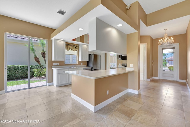 kitchen with stainless steel appliances, an inviting chandelier, kitchen peninsula, pendant lighting, and white cabinets