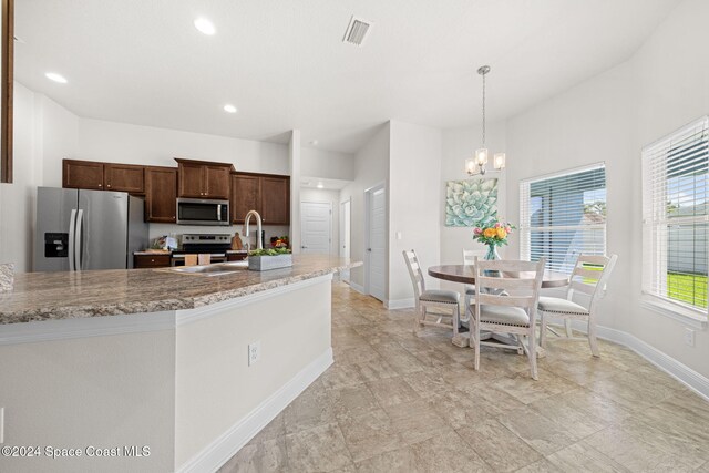 kitchen featuring light stone counters, sink, pendant lighting, and appliances with stainless steel finishes