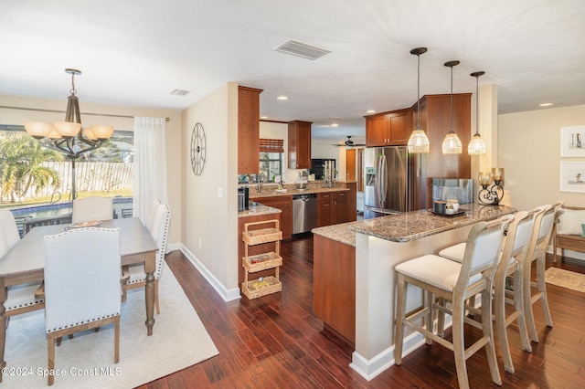 kitchen with kitchen peninsula, appliances with stainless steel finishes, decorative light fixtures, and light stone counters