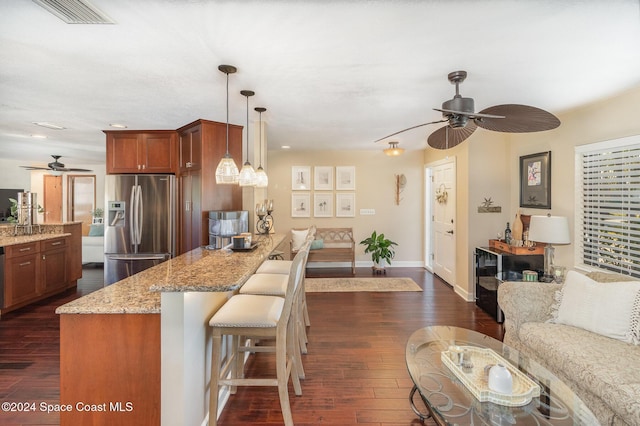 kitchen featuring light stone countertops, hanging light fixtures, a kitchen breakfast bar, stainless steel fridge with ice dispenser, and dark hardwood / wood-style flooring