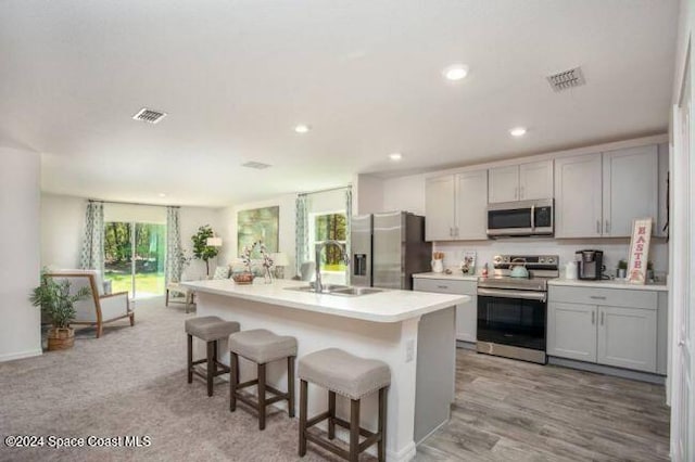 kitchen featuring appliances with stainless steel finishes, a breakfast bar, a kitchen island with sink, sink, and light hardwood / wood-style floors