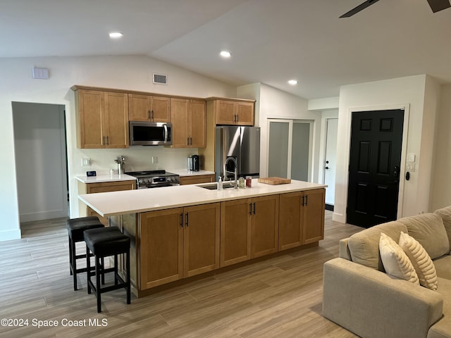 kitchen with sink, stainless steel appliances, an island with sink, lofted ceiling, and light wood-type flooring