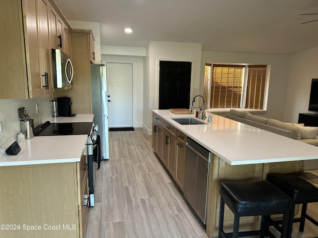 kitchen featuring sink, light wood-type flooring, an island with sink, a kitchen bar, and stainless steel appliances