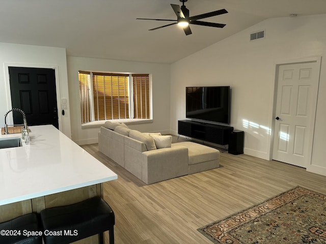 living room with ceiling fan, sink, light hardwood / wood-style flooring, and vaulted ceiling