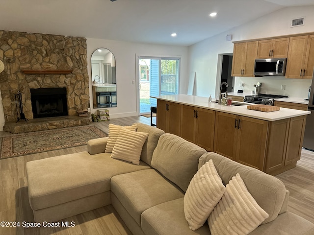 kitchen with sink, vaulted ceiling, light wood-type flooring, a fireplace, and stainless steel appliances