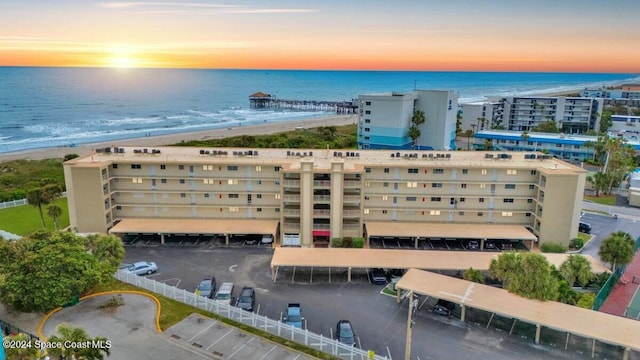 aerial view at dusk featuring a water view and a beach view