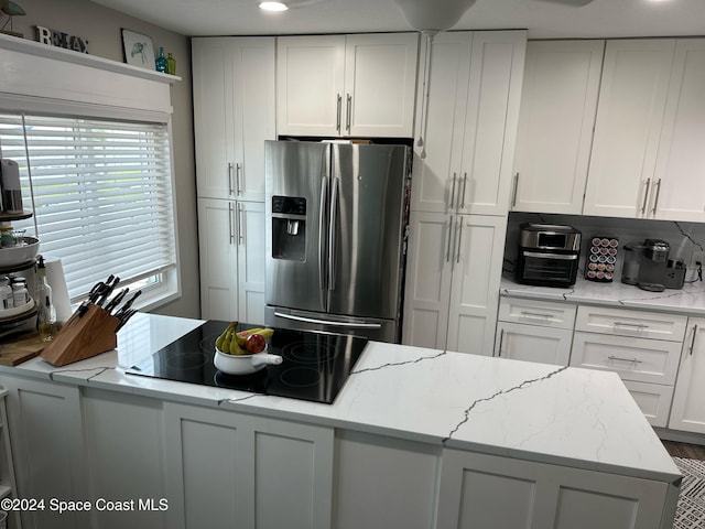 kitchen featuring stainless steel refrigerator with ice dispenser, light stone counters, white cabinets, and black electric cooktop