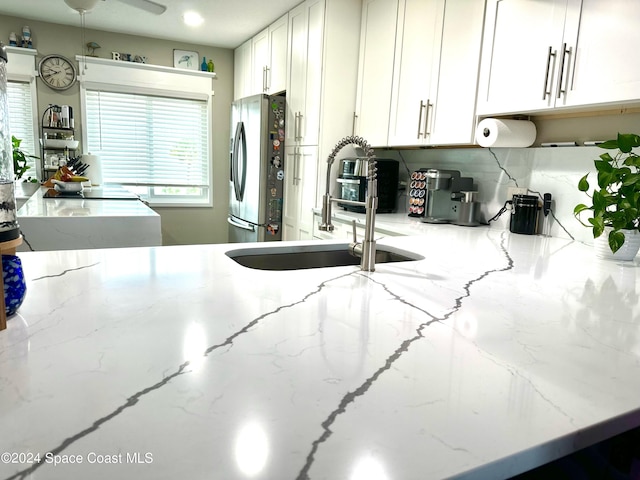 kitchen with light stone countertops, sink, and stainless steel refrigerator