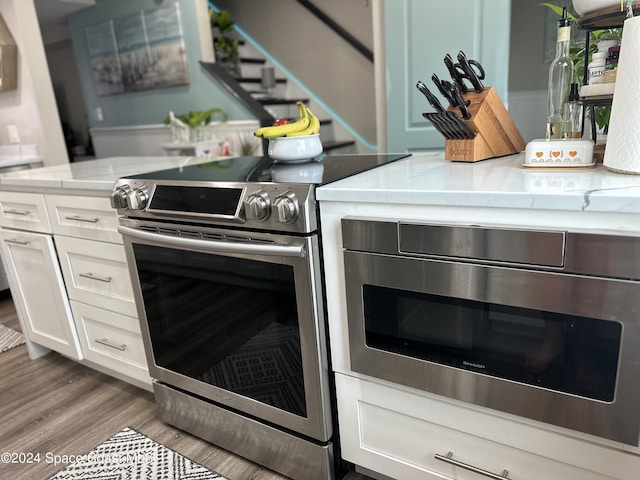 kitchen featuring wall oven, stainless steel electric range, wood-type flooring, and white cabinets