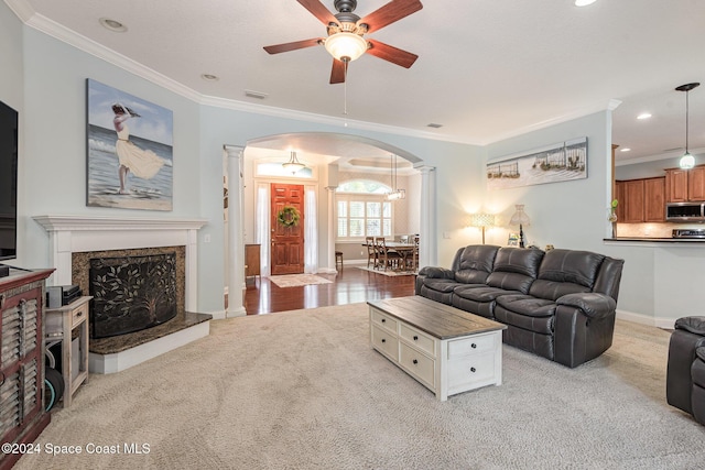 carpeted living room with a fireplace, ornate columns, ceiling fan, and ornamental molding