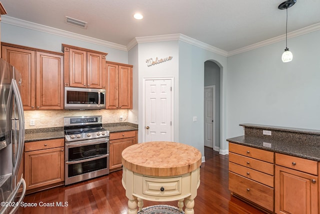 kitchen with hanging light fixtures, stainless steel appliances, backsplash, dark stone countertops, and ornamental molding