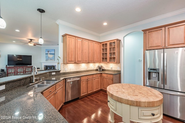 kitchen with backsplash, dark stone counters, sink, hanging light fixtures, and stainless steel appliances