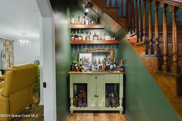 bar with hardwood / wood-style flooring, a notable chandelier, green cabinets, and crown molding