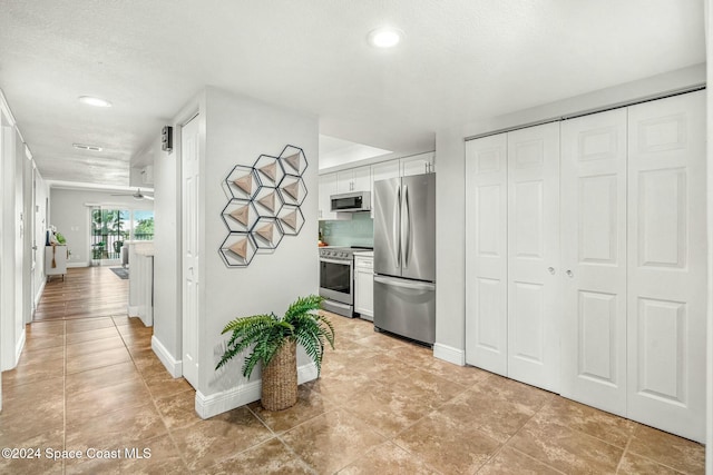 kitchen with light tile patterned floors, white cabinets, a textured ceiling, and appliances with stainless steel finishes