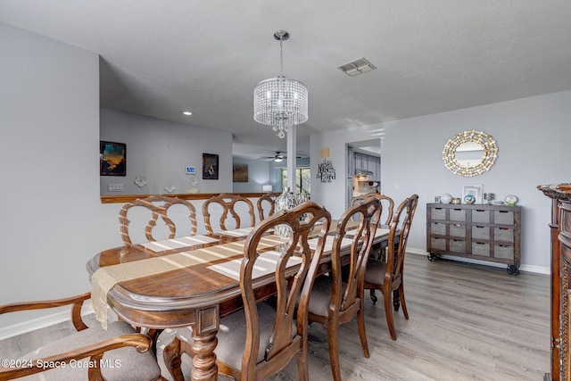 dining room with a textured ceiling, ceiling fan with notable chandelier, and light wood-type flooring