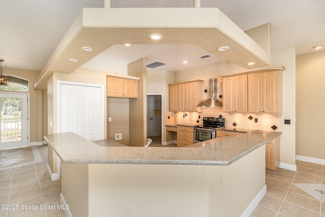 kitchen with light brown cabinetry, tasteful backsplash, stainless steel range with electric stovetop, wall chimney range hood, and an inviting chandelier