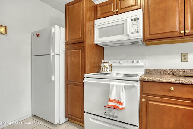 kitchen featuring a textured ceiling, light stone counters, light tile patterned floors, and white appliances