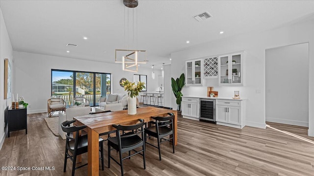 dining room featuring a dry bar, light wood finished floors, beverage cooler, and visible vents