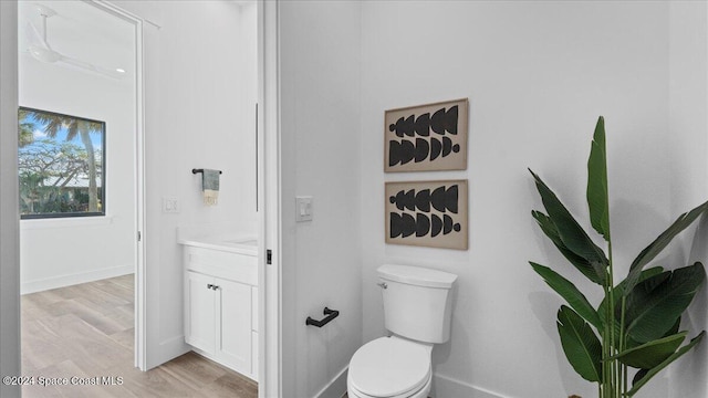 bathroom featuring toilet, baseboards, wood finished floors, and vanity