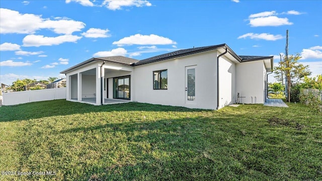 rear view of house with stucco siding, fence, a sunroom, and a yard