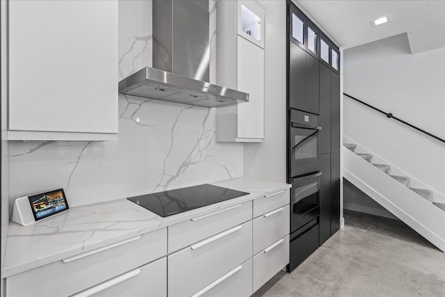 kitchen featuring black electric stovetop, white cabinetry, light stone countertops, and wall chimney range hood