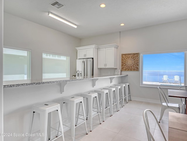 kitchen featuring white cabinets, light tile patterned floors, light stone counters, a kitchen bar, and stainless steel fridge with ice dispenser