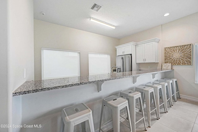 kitchen with white cabinets, stainless steel refrigerator with ice dispenser, kitchen peninsula, a breakfast bar area, and light tile patterned floors