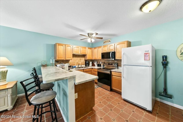 22 Tulip Ave Unit 309, Cocoa Beach, FL 32931 - kitchen with stainless steel appliances, a kitchen bar, light brown cabinetry, a peninsula, and a textured ceiling