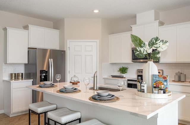 kitchen with backsplash, sink, an island with sink, white cabinetry, and stainless steel appliances